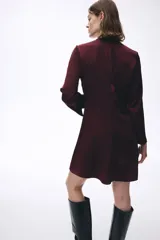 Vestido corto de color bordó, con escote redondo y detalle girado en el frente. Presenta mangas largas con abertura en los puños, falda con leve vuelo y cierre oculto en la espalda.