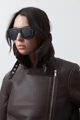 Campera tipo gamulán de símil cuero color marrón oscuro, con interior y solapas de corderito al tono. Presenta cierre frontal cruzado, bolsillos con cierre metálico y hebilla ajustable en el cuello.
