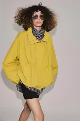 Cazadora bomber de cuello subido ajustable con cordones, manga larga con puños elásticos y cierre frontal con cremallera y botones a presión ocultos bajo solapa. Cuenta con bolsillos delanteros y diseño holgado.