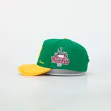 Gorra tipo baseball de color verde con visera amarilla. Presenta una letra B bordada en amarillo en el frente, la palabra Desires bordada en el lateral y un parche con diseño urbano y logo de la marca en el otro lateral.