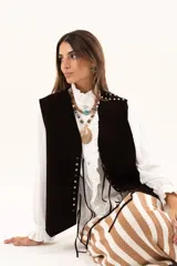 Chaleco oversize confeccionado en cuero descarne, con diseño de terminación en picos. Presenta lazos frontales con ojalillos metálicos y detalle de tachas metálicas en hombros y espalda.