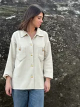 Camisa color crema tejida en lana, con cuello clásico, cierre frontal con botones dorados, dos bolsillos con solapa en el pecho y mangas largas con puños abotonados.