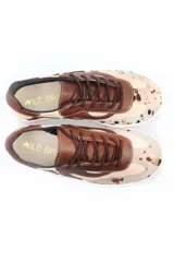Championes de cuero con diseño de paneles orgánicos en tonos tierra. Presenta una combinación de cuero liso marrón y beige, con detalle de cuero con pelo estampado tipo vaca en la puntera. Cuenta con cordones al tono y suela blanca.
