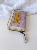 Billetera pequeña con cierre metálico, cuerpo principal de cuero lila texturizado y ribetes en color crema. Presenta un parche de cuero marrón con la palabra "chowie" escrita en cursiva.
