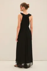 Vestido largo de gasa color negro, con escote profundo adornado con volados, lazos en el cuello con terminaciones metálicas y corte en la cintura con cinturón a tono.