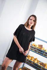 Vestido corto negro de tejido calado con patrón cuadrado, corte oversized, cuello redondo y mangas cortas. Presenta terminaciones a contratono en escote y mangas, y un logo bordado a mano en el frente.