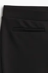 Pantalón de tiro alto confeccionado en punto roma, con diseño ajustado en la parte superior y piernas acampanadas. Presenta bolsillos insertados decorativos en la parte frontal.