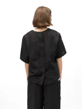 Remera de lino con corte holgado, cuello redondo y mangas cortas. Presenta un diseño minimalista con detalle de botones en la espalda.