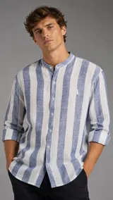 Camisa de lino con cuello mao y rayas anchas verticales en tonos azul y blanco, de manga larga con puños arremangados y cierre frontal con botones.
