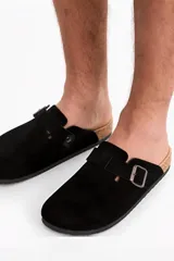 Zueco tipo slip-on color negro con tira y hebilla metálica regulable, diseño cerrado en la parte delantera y suela de corcho.