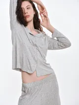 Camisa de pijama de manga larga con cuello solapa y cierre frontal de botones. Presenta un estampado sutil de pequeños corazones sobre una base de color gris melange, con detalles de ribete en contraste en el cuello y la botonera.