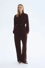 Blazer oversized bordó de cuello alto, con hombreras, bolsillos delanteros ribeteados, abertura en los puños y cinturón fino incorporado con hebilla metálica.