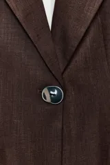 Blazer marrón confeccionada en hilatura con mezcla de lino, con cuello solapa, manga larga, bolsillos con solapa en el delantero y cierre frontal con un botón. Cuenta con forro interior en color blanco contrastante.