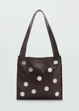Bolso tipo shopper color marrón oscuro de cuero con apliques circulares plateados. Tiene doble asa de hombro y cierre magnético.