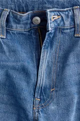 Jeans de cinco bolsillos en denim de algodón con leve stretch, de tiro alto y corte ajustado desde la cintura hasta el muslo, ensanchándose de la rodilla hacia abajo (bootcut). Presenta cierre y botón frontal.