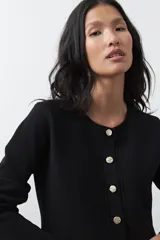 Cardigan negro de tejido de punto con cuello redondo y cierre frontal con botones a contraste. Presenta un corte entallado en la cintura con una silueta levemente evasé y mangas largas.