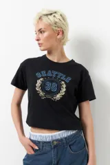 Remera negra de manga corta y corte clásico, con estampa azul de la palabra "Seattle" con estrellas y el número 38 en el centro, rodeado de laureles.