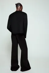 Pantalón de tiro alto con diseño flare, confeccionado en tela de color negro. Presenta cinco bolsillos, cintura con trabillas y cierre frontal con cremallera y botón.