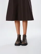 Botas de caña baja con punta cuadrada, confeccionadas en una combinación de cuero liso y gamuza en tonos marrones oscuros. Presentan un diseño de paneles con costuras visibles, elásticos laterales y una suela track robusta.