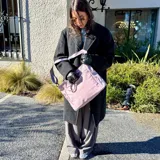 Bolso tipo tote color gris claro, con doble asa de mano y correa larga regulable. Tiene dos bolsillos laterales y un bolsillo frontal.