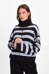 Campera de punto holgada con cuello tipo chomba y cierre frontal oculto. Presenta un diseño de rayas horizontales en tonos marrón, rojo y crema, con puños y ruedo acanalados. Incluye un parche bordado en la manga izquierda.