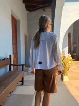 Camisa blanca de corte holgado con cuello bebé con volados, cierre frontal de botones y mangas largas con puños terminados en volados.