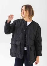 Chaqueta acolchada de color negro con diseño de costuras onduladas. Presenta cuello redondo, cierre frontal con botones a presión y dos bolsillos frontales tipo cargo con solapa y detalle de hebilla. Posee un corte holgado y mangas largas.