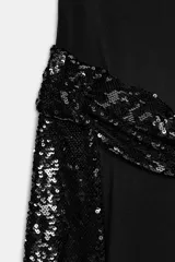 Vestido midi negro de cuello subido y manga corta amplia, con espalda descubierta. Presenta un fajín drapeado con lentejuelas negras a tono en la cadera y abertura lateral en el bajo.