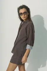 Camisa de corte relajado con diseño de rayas verticales en tonos rojos, marrones y blancos. Presenta cuello clásico, cierre frontal con botones al tono y mangas largas con puños que permiten un estilo arremangado.