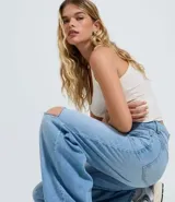 Pantalón de jean modelo wide leg en color azul medio, con cintura baja y corte holgado. Presenta roturas decorativas en las rodillas, bolsillos funcionales, cierre frontal con botón y cremallera, y trabillas para cinturón.