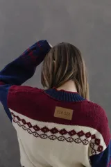 Campera tipo bomber tejida en lana 100% merino, con diseño artesanal que combina guardas estilo patagónicas y motivos florales. Presenta cierre frontal tipo diente de perro y terminaciones en tejido acanalado en puños, cuello y ruedo.