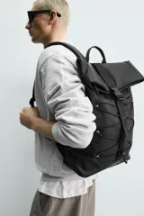 Mochila técnica de acabado engomado en color negro. Presenta un diseño de solapa con cierre de hebilla de liberación rápida y un sistema de cordones elásticos frontales. Incluye compartimento para dispositivos electrónicos, espalda acolchada y correas ajustables.