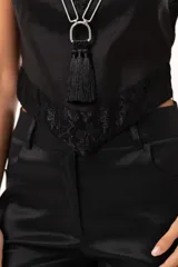 Top de satén negro con escote en V, decorado con detalles de encaje floral en el escote y en el ruedo. Presenta breteles finos ajustables y un corte asimétrico en la parte inferior.