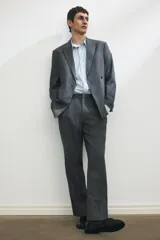 Blazer cruzado de color gris medio, con solapas de pico, ojal decorativo y cierre de doble botonadura. Presenta bolsillo superior insertado, bolsillos delanteros ribeteados con solapa y botones decorativos en los puños.