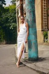 Vestido midi de lino con cuello halter y escote en pico. Presenta un diseño con frunces en el delantero, abertura lateral y cierre posterior con cremallera oculta y botones.