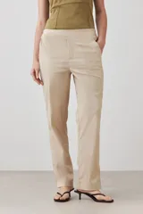 Pantalón de corte recto y tiro medio, confeccionado en tela de gabardina color beige. Presenta cierre frontal con cremallera y botón oculto, bolsillos laterales y costuras verticales decorativas en la parte superior.