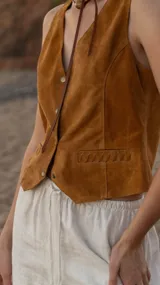Chaleco marrón de gamuza con cuello en V, cierre con botones y bolsillos frontales con detalle de costuras. Corte recto.