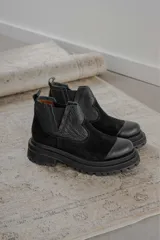 Bota tipo chelsea de caña baja, confeccionada en una combinación de cuero texturizado y gamuza negra. Presenta punta redonda reforzada, elásticos laterales y una suela track robusta de goma.