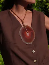 Collar con dije de piedra ágata blanca y marrón, con forma circular irregular y agujero en el centro. El dije está sujeto con un cordón fino de cuero marrón.