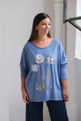 Remera de algodón color celeste, con cuello redondo amplio, mangas largas y estampa frontal de flores en tonos blanco y dorado.
