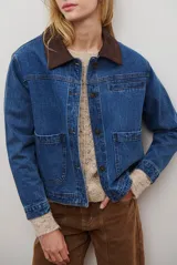 Chaqueta de jean azul con cuello de gamuza color camel, bolsillos delanteros y cierre de botones.