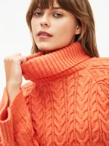 Polerón de tejido de punto color gris claro, con cuello alto y diseño de trenzas en el cuerpo y mangas. Corte holgado y puños anchos.