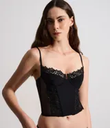Corset de media copa en color blanco, confeccionado con paneles de poliamida y detalles decorativos de encaje floral en el borde superior y tul en los laterales. Cuenta con tirantes finos ajustables y varillas internas para estructura.