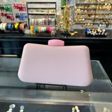 Clutch de rafia sintética color rosa suave, con cierre a tono y asa desmontable de cadena dorada. Incluye borla decorativa.