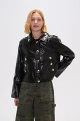 Chaqueta corta de eco-cuero negra con cuello camisero, cierre frontal con botones plateados y bolsillos simulados con botones plateados.