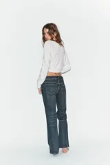 Jeans de tiro bajo con corte bootcut, confeccionados en denim con efecto lavado. Presentan costuras verticales marcadas en el frente, cierre frontal con cremallera, gancho metálico y detalle de trabilla con botones en la cintura.