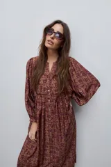 Vestido largo de silueta amplia y caída fluida, con estampado y recortes fruncidos que aportan movimiento. Presenta escote con abertura, cierre frontal con botones y mangas largas de volumen amplio con puños elastizados.