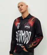 Remera de manga larga con corte boxy, confeccionada en microfibra de poliéster. Presenta un diseño estampado con motivos de llamas en tonos rojos y naranjas, junto con el número 13 en tipografía gótica en la espalda.