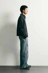 Chaqueta cropped fit de denim de algodón en color negro con efecto lavado, cuello mao y cierre frontal con cremallera. Presenta aplicaciones de trabillas horizontales en el pecho y en las mangas, además de hombreras abotonadas.