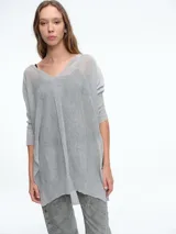 Sweater tipo túnica de tejido liviano con sutil transparencia y acabado brillante. Presenta escote en V, mangas largas relajadas y un corte amplio con largo asimétrico.